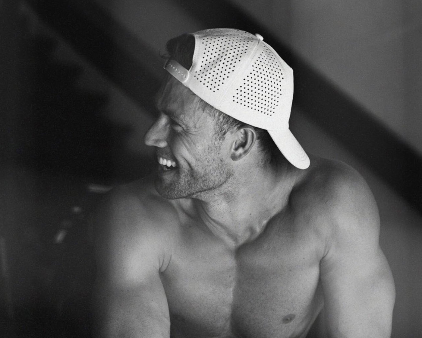 Smiling shirtless man in side profile wearing a white perforated backward baseball cap (black-and-white photo) - Daily Tech Hat Grey