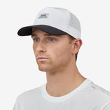 A man angled wearing a white baseball cap with a black brim and a small rectangular 'Nostrand' logo patch on the front, paired with a white t-shirt against a light gray background.