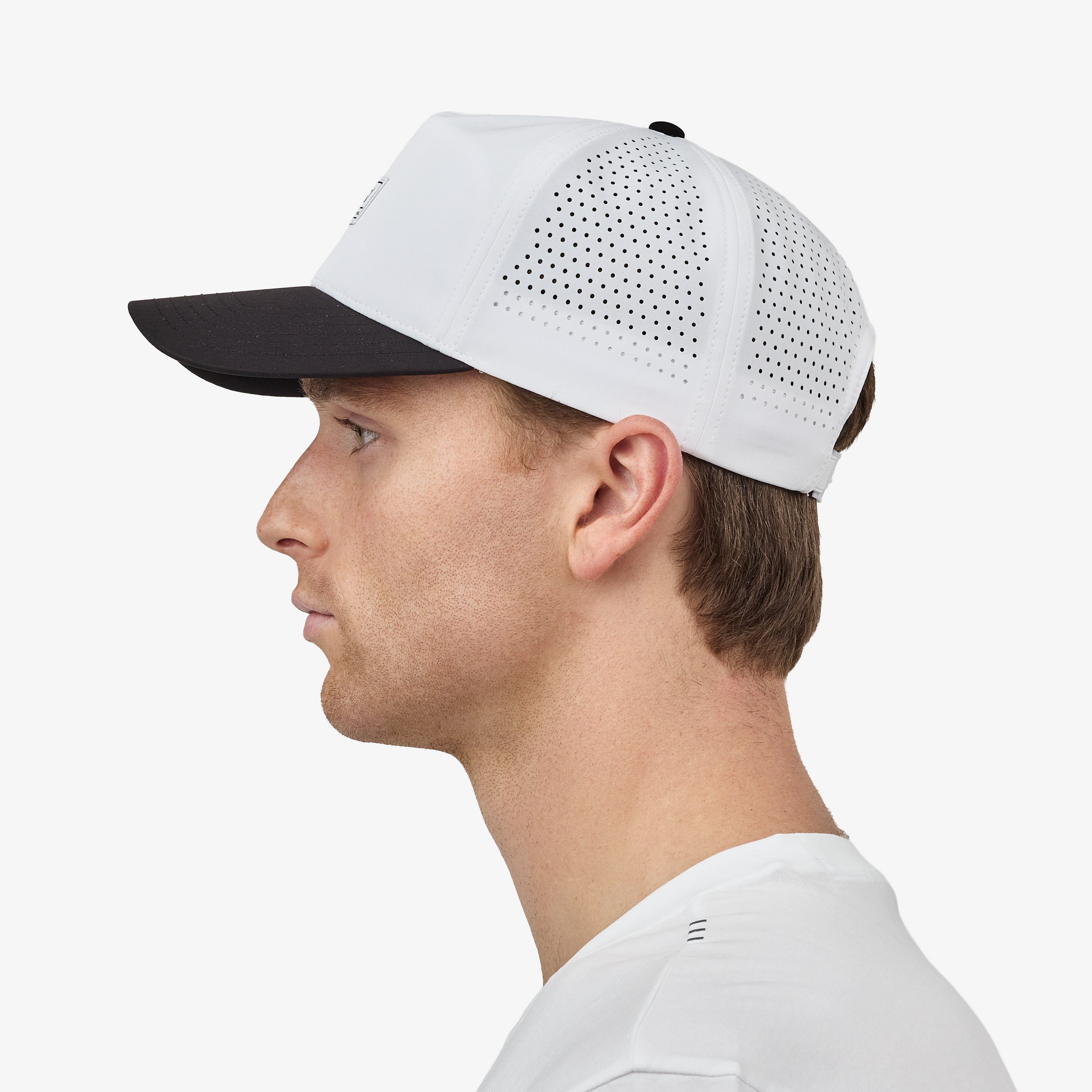 A man profiled wearing a white baseball cap with a black brim and a small rectangular 'Nostrand' logo patch on the front, paired with a white t-shirt against a light gray background.